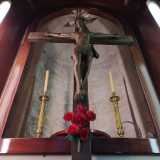 Riproduce il classico Cristo morente, con piccoli motivi dorati che decorano gli assi in corrispondenza delle mani e della testa. Affianco sono stati poi aggiunti due candelabri e al di sotto un mazzo di rose rosse